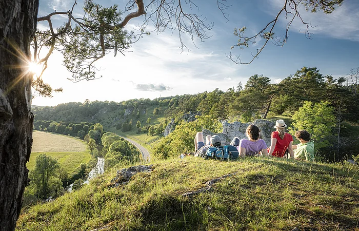 Vier Wanderer liegen im grünen auf den 12 Aposteln am Altmühltal-Panoramaweg. Sie genießen den Sonnenuntergang und den Blick ins Tal.